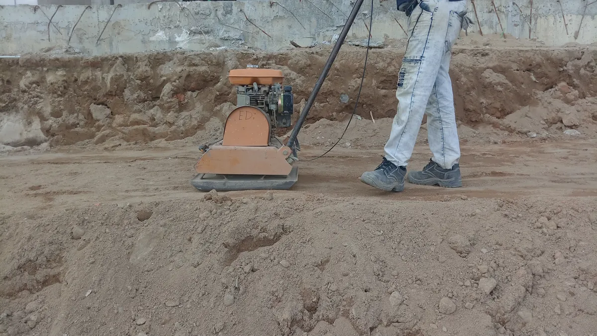 Worker compacting dirt with a plate compactor