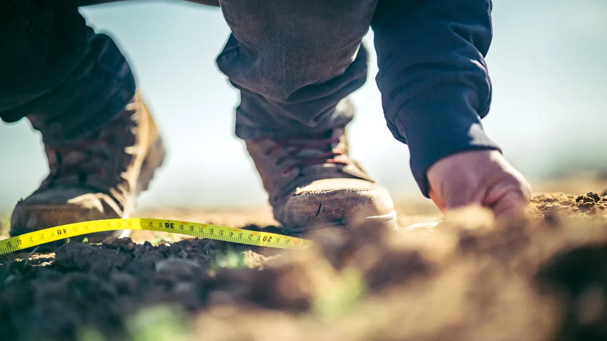 boots and hands measuring ground with a tape measure
