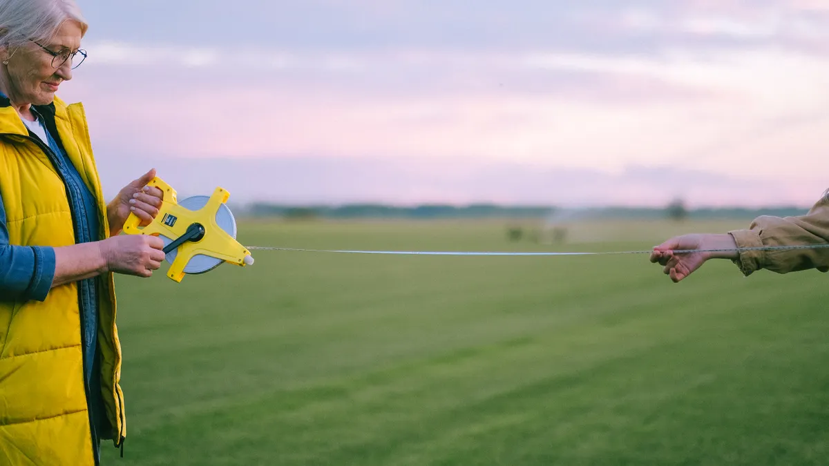 two people holding a tape measure across a grassy field