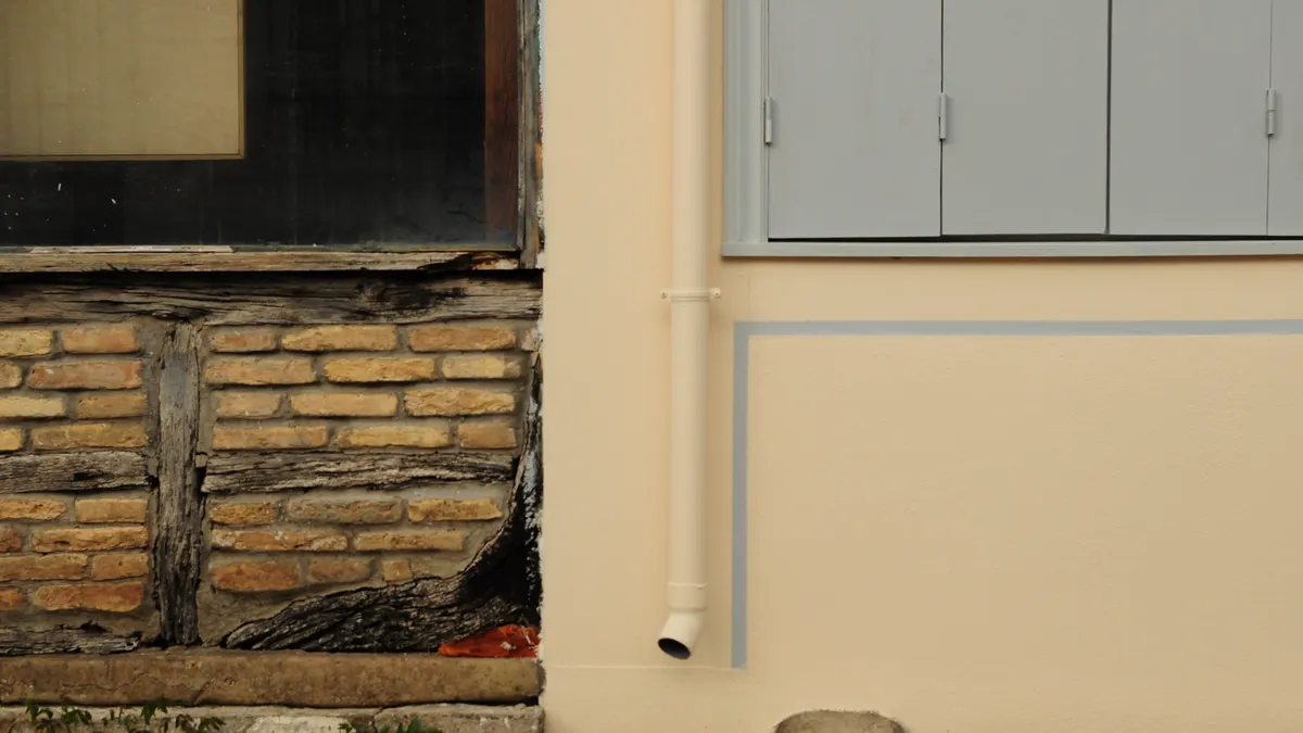 House foundation wall with damaged lower brick and downspout